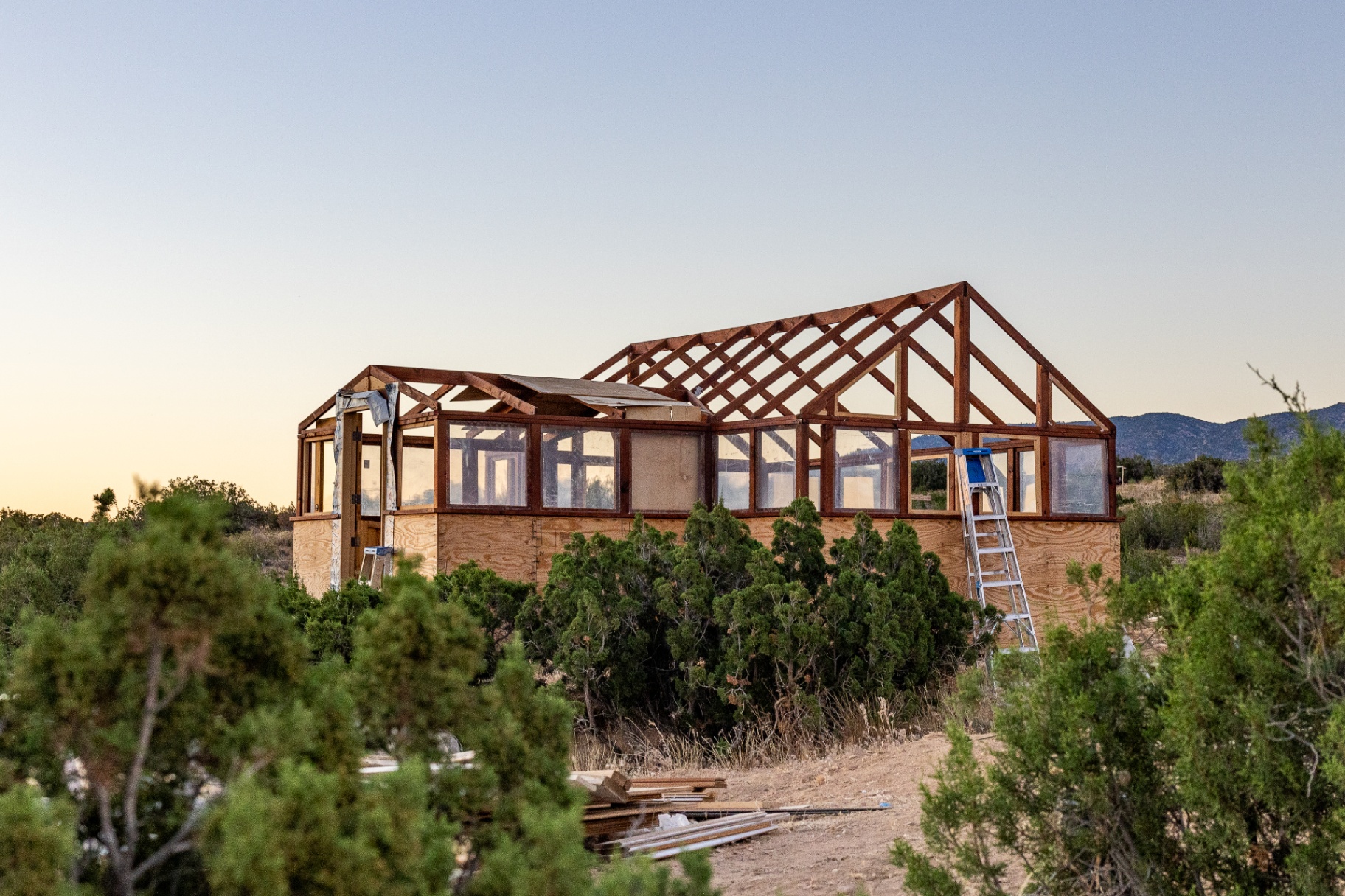 Greenhouse structure at dusk with wooden trusses, installed panels, and a ladder