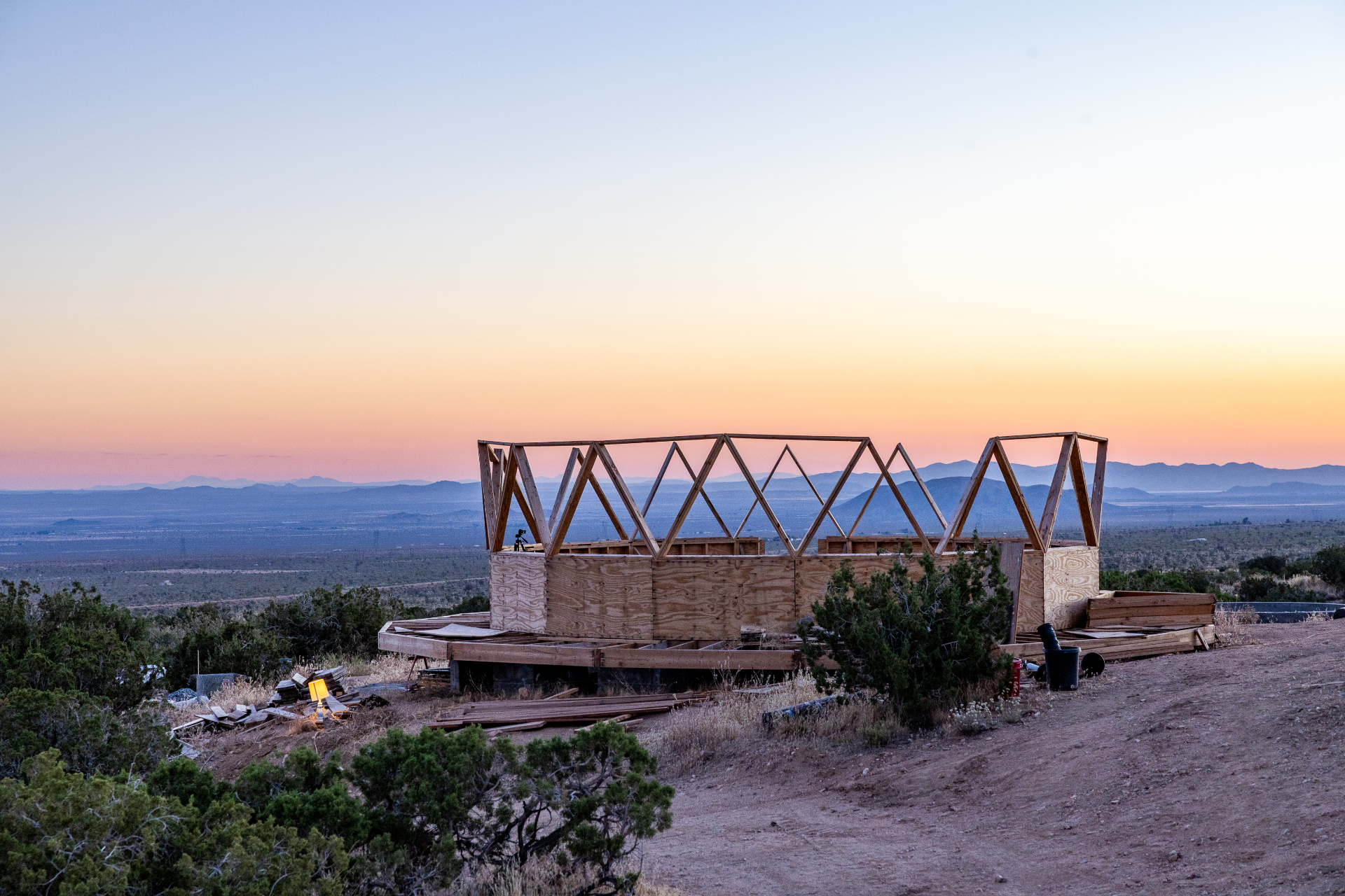 Wooden geodesic Dome House frame on its concrete foundation at sunset, high desert in the distance